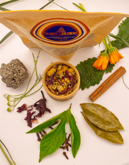 Chamomillionaire Tea package surrounded by Pyrite crystal, cinnamon, chamomile, hibiscus, passionflower, wood betony, calendula, and bay leaf.