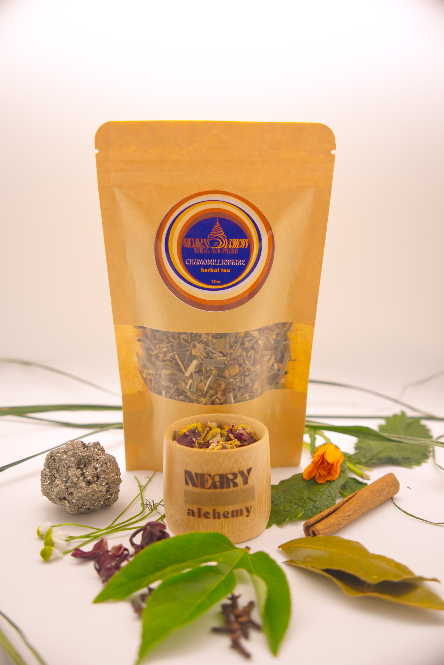 Chamomillionaire Tea package surrounded by Pyrite crystal, cinnamon, chamomile, hibiscus, passionflower, wood betony, calendula, and bay leaf.