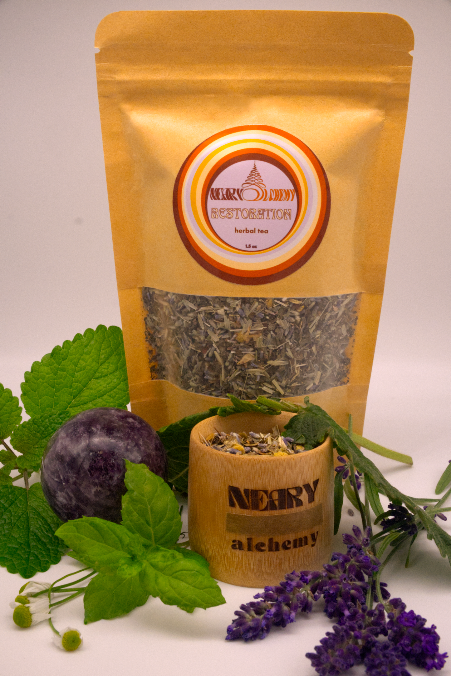 Restoration Herbal Tea package surrounded by lemon balm, peppermint, lavender, and other herbs with Lepidolite crystal sphere.