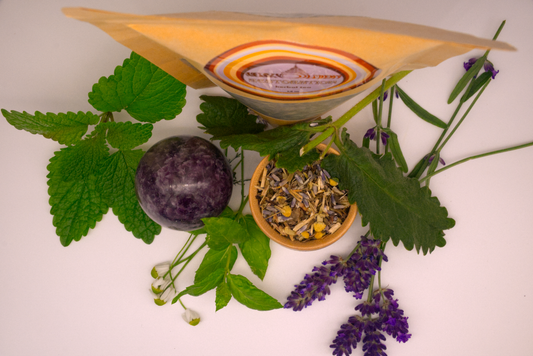 Restoration Herbal Tea package surrounded by lemon balm, peppermint, lavender, and other herbs with Lepidolite crystal sphere.