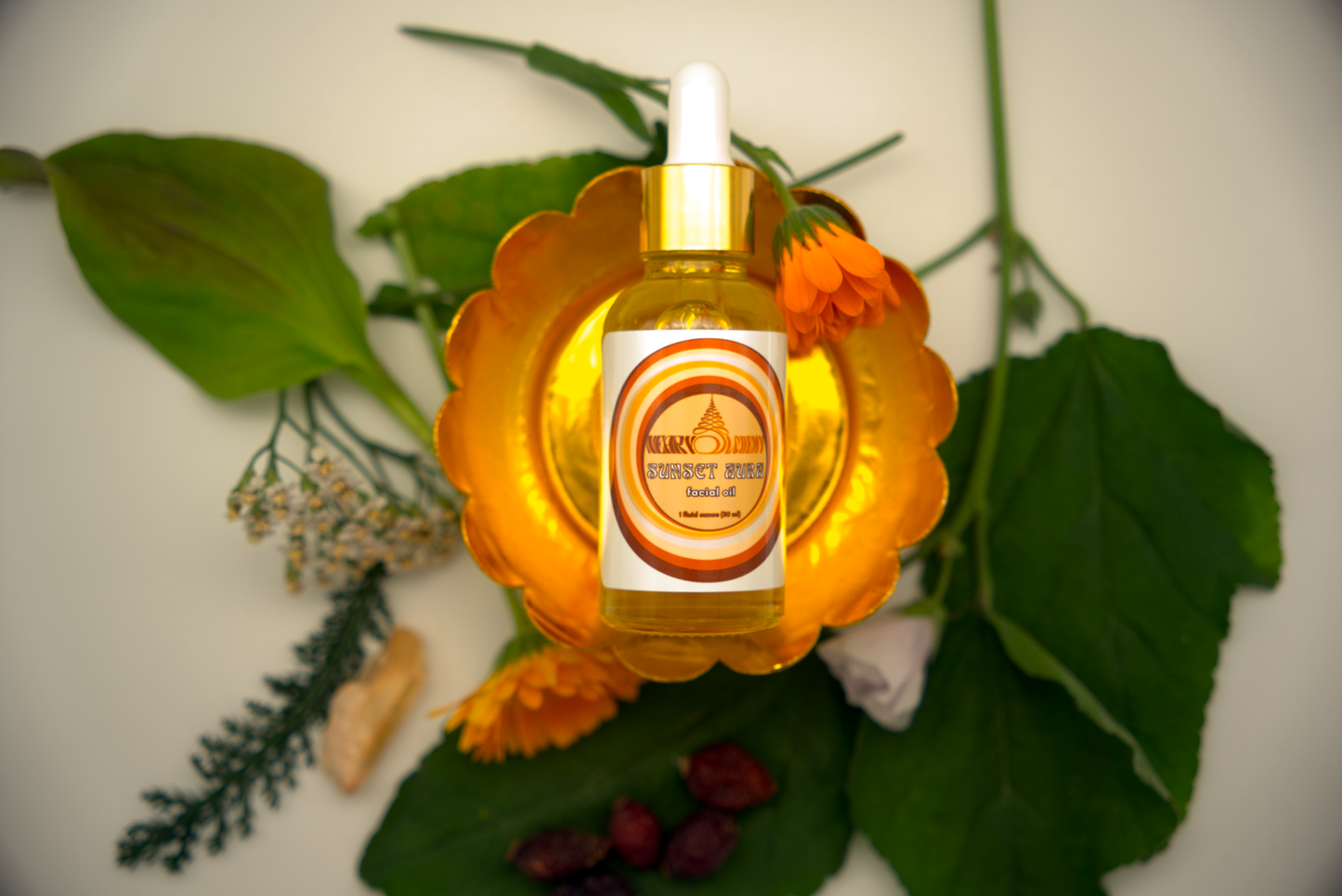 Bottle of Sunset Aura Facial Oil on decorative stand surrounded by herbs and Sunset Aura crystal.
