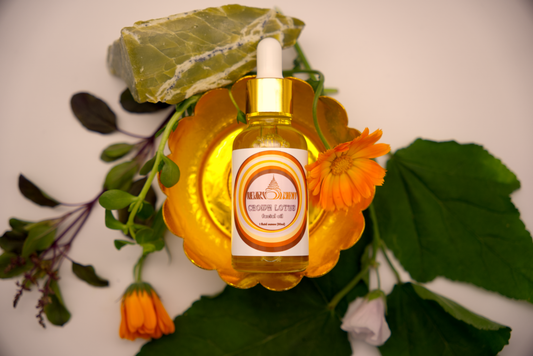 A bottle of Crown Lotus Facial Oil  placed on a decorative container, surrounded by herbs and Serpentine crystal.