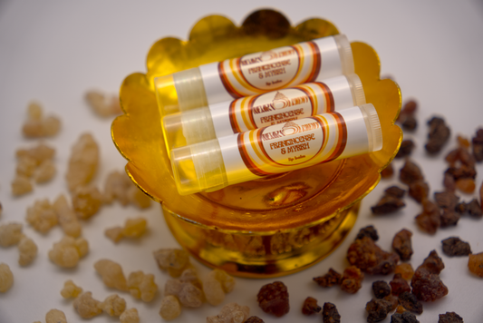 Frankincense and Myrrh lip balm on gold stand with frankincense and myrrh resin scattered around it.