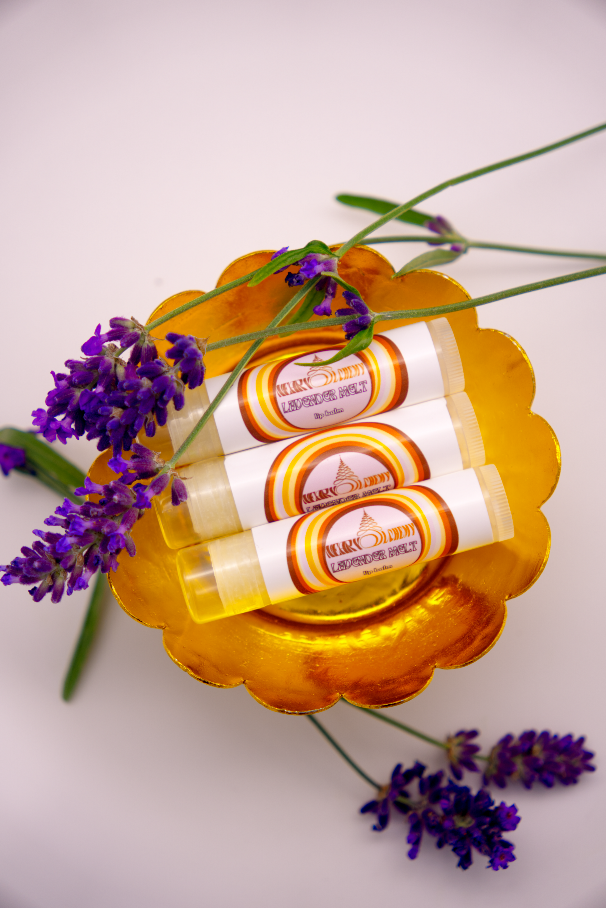 Three Lavender Melt lip balms in a decorative holder with lavender flowers on a light background