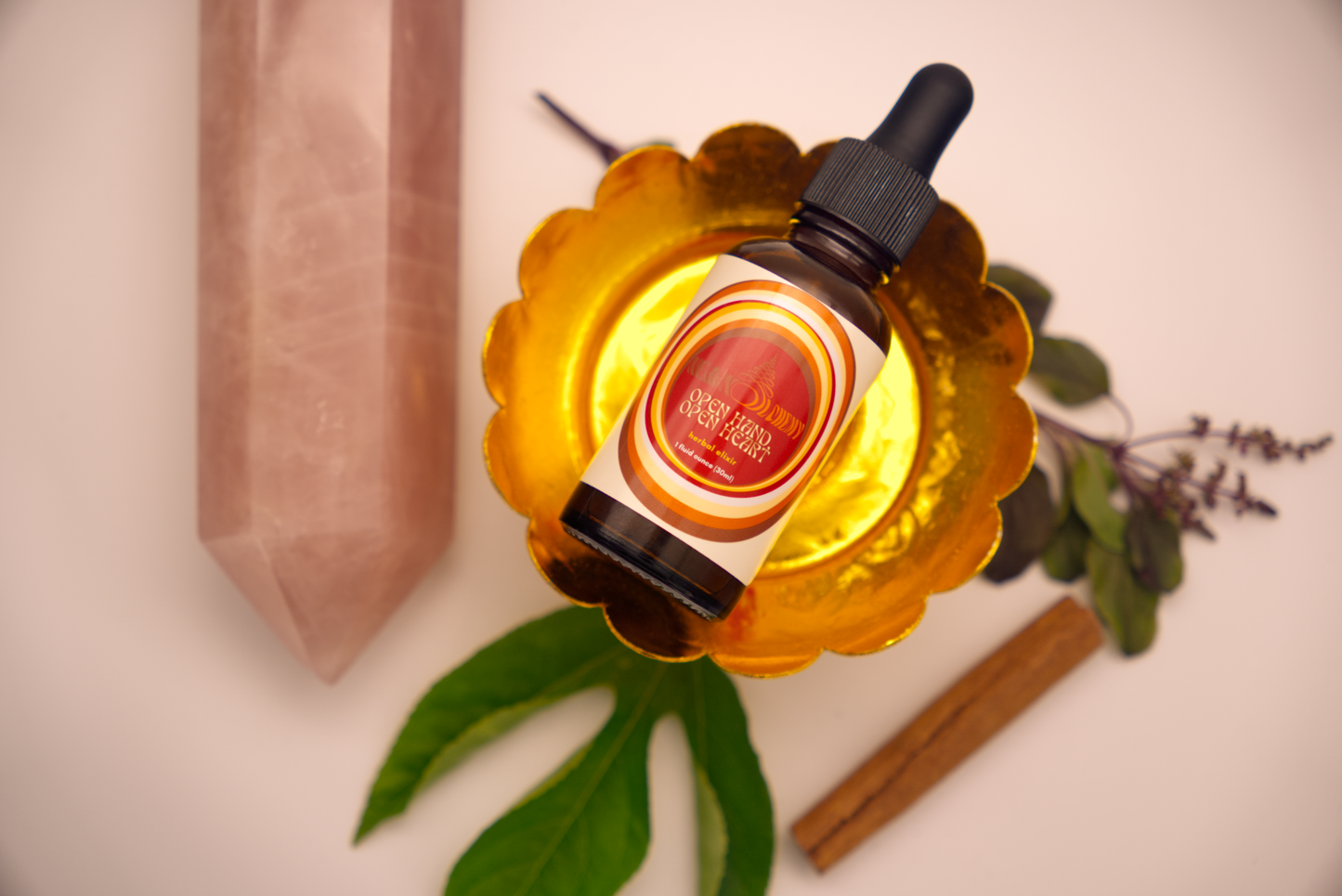 Open Hand, Open Heart Elixir on decorative stand surrounded by herbs and rose quartz crystal.