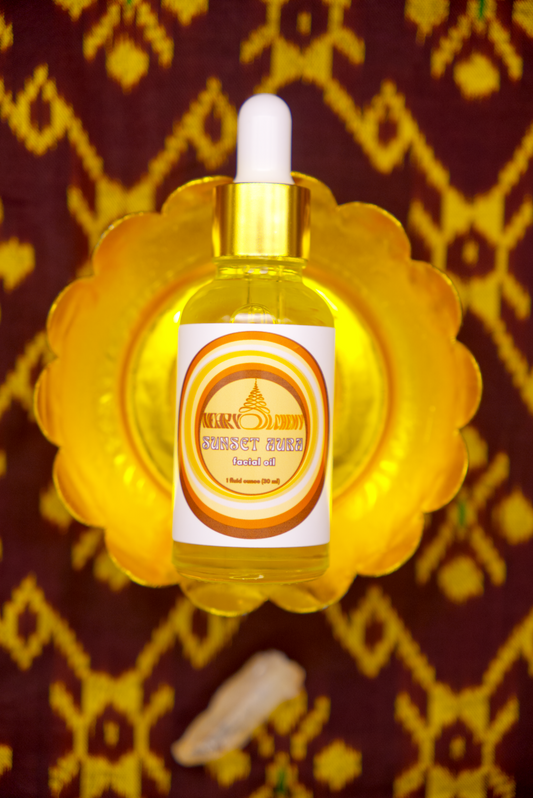 Bottle of Sunset Aura Facial Oil on decorative stand with Khmer silk fabric background and Sunset Aura crystal.