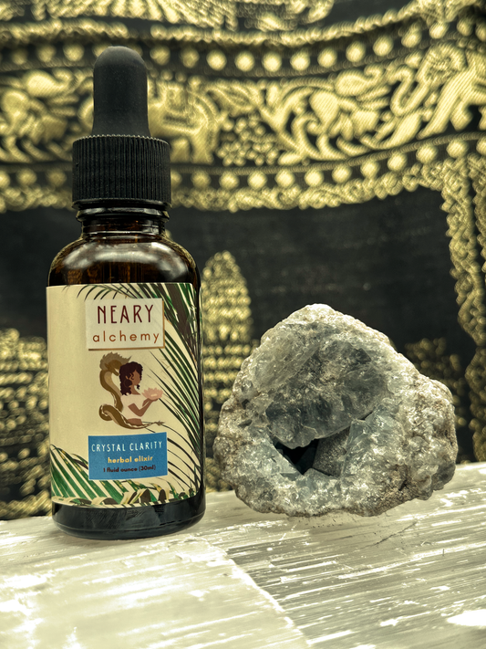 An amber colored tincture bottle with the label, "Crystal Clarity Herbal Elixir" written in a blue box, placed next to a Celestite crystal.