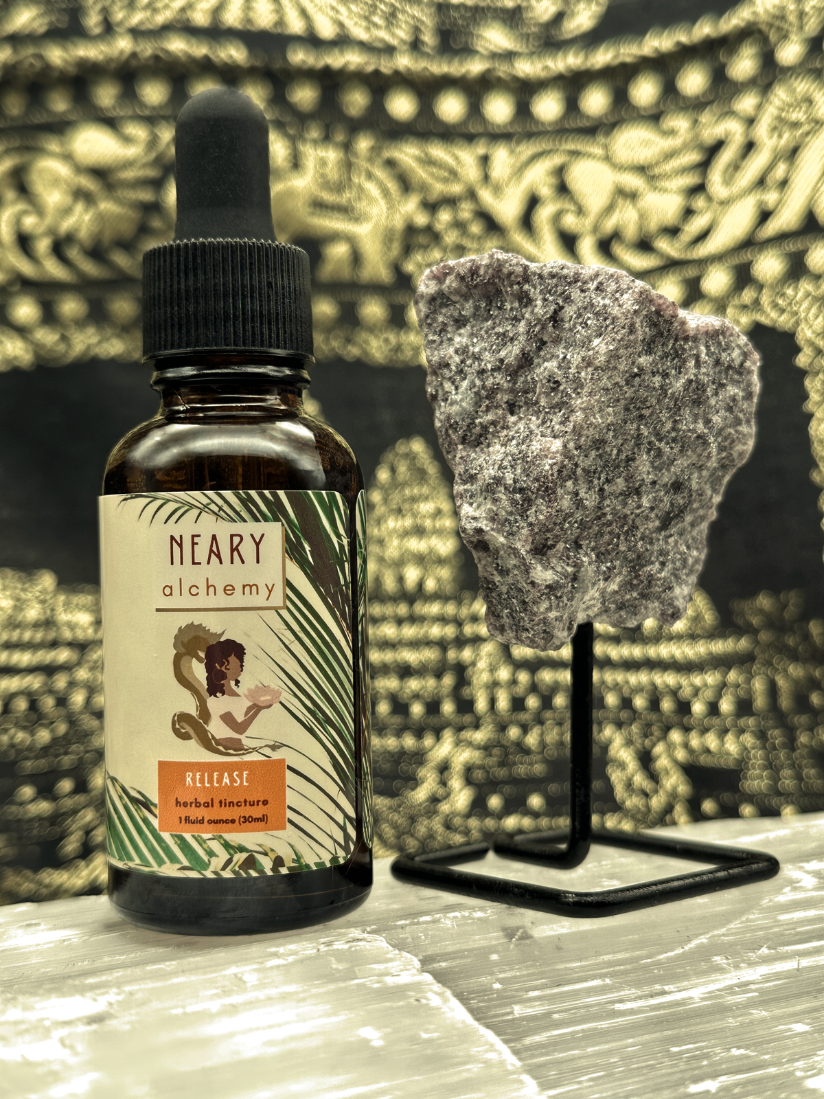 An amber colored tincture bottle with the label "Release Herbal Elixir" placed next to a Lepidolite crystal.